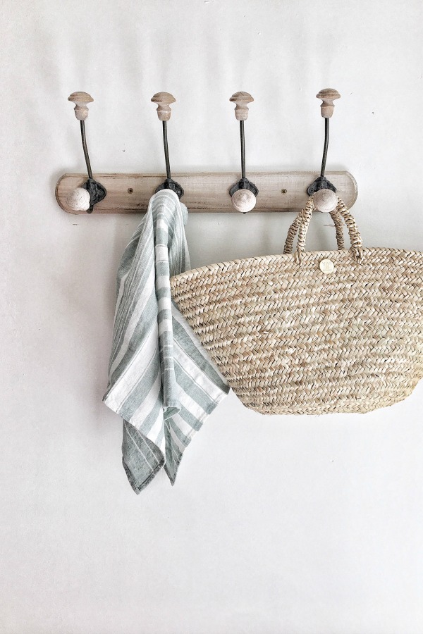 French farmhouse splendor in a kitchen with a French market basket and linen towel hanging from a rustic wall rack. Vivi et Margot. Come score ideas for 16 Amazing Serene Paint Colors Interior Designers Use for a Soothing Vibe.