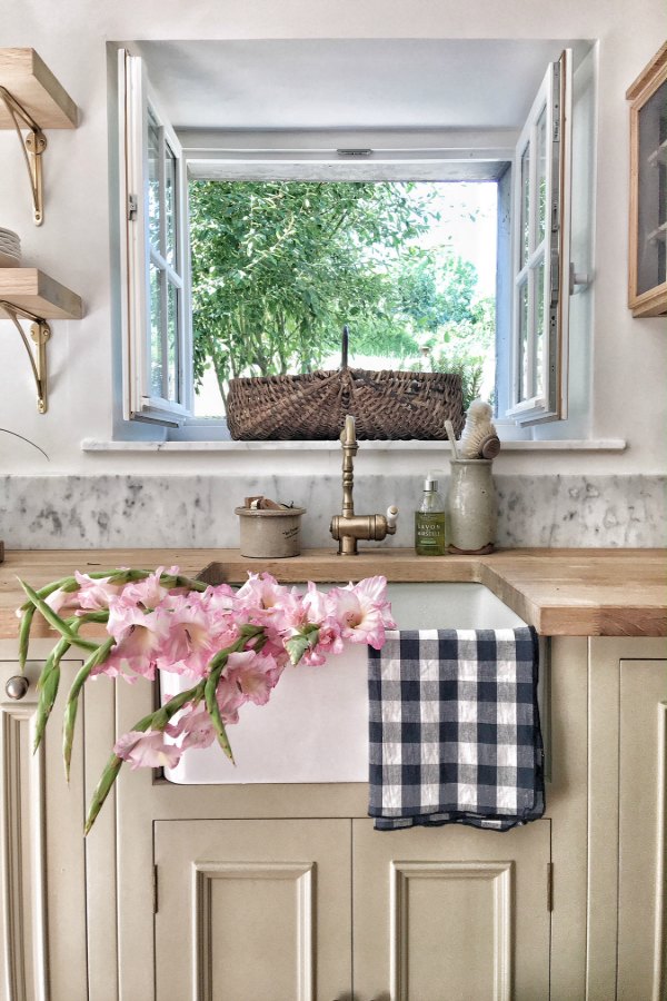 Farm sink in an authentically renovated French farmhouse kitchen near Bordeaux, France, by Vivi et Margot features reclaimed terracotta hex tile floors, rustic ceiling beams, and a custom kitchen by Neptune.