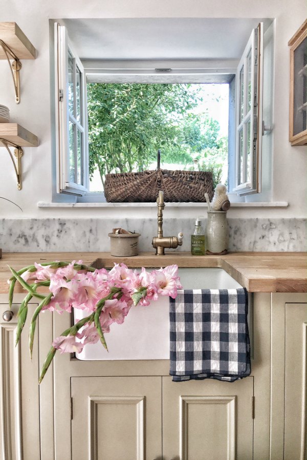 Farm sink in an authentically renovated French farmhouse kitchen near Bordeaux, France, by Vivi et Margot features reclaimed terracotta hex tile floors, rustic ceiling beams, and a custom kitchen by Neptune.