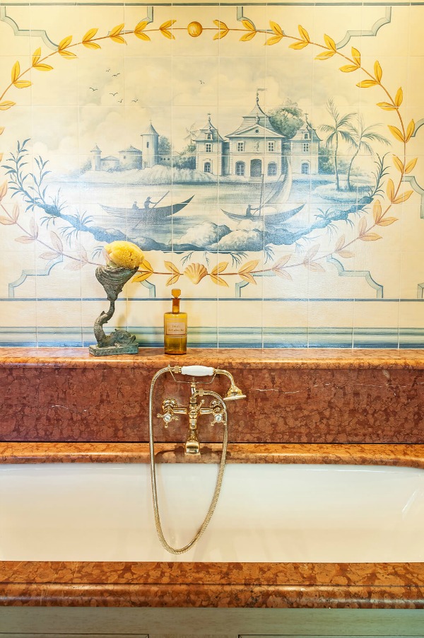 Beautiful tiled mural and detail of of a bath's stone surround and brass fixtures in an elegant French chateau - Haven In.