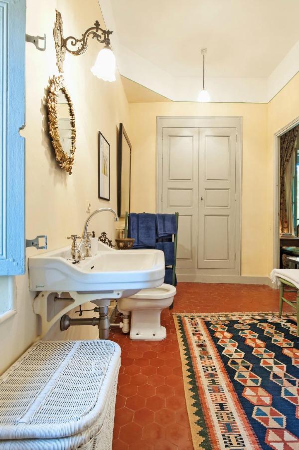 Traditional French bathroom with terracotta hex tile flooring, yellow walls, and colorful area rug - Haven In.