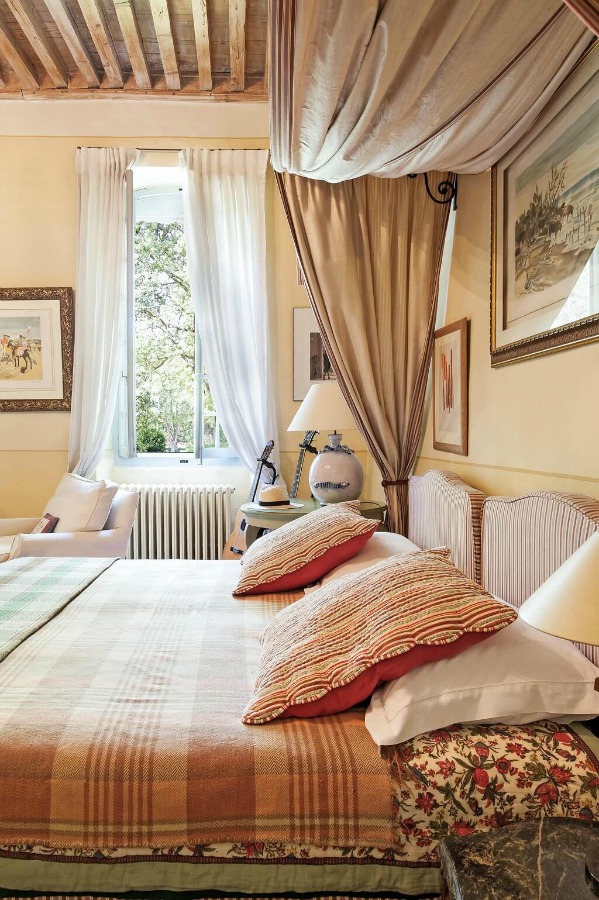 Restful, elegant, and traditional, this French country bedroom in a luxurious historical villa features pale yellow walls and soft earthy reds - Haven In. #frenchcountry #bedrooms