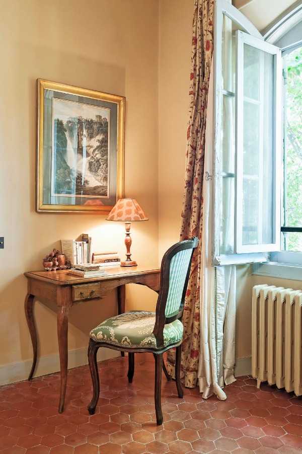 Goldenrod walls and terracotta hex tiled floor in a Provence bedroom with writing desk area and inswing windows - Haven In.