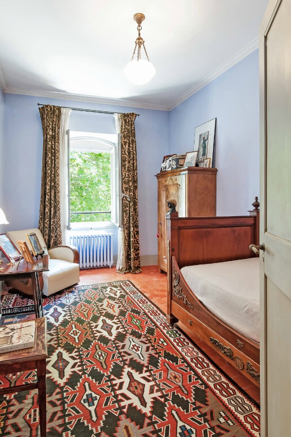 Cool blue walls in a Provence bedroom with terracotta tile floors and earthy red area rug - Haven In.