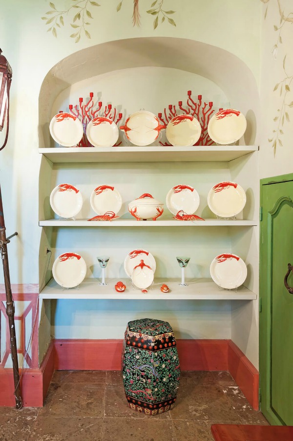 Shelves of beautiful plates displayed in a traditional French dining room with red and green accents in Provence.