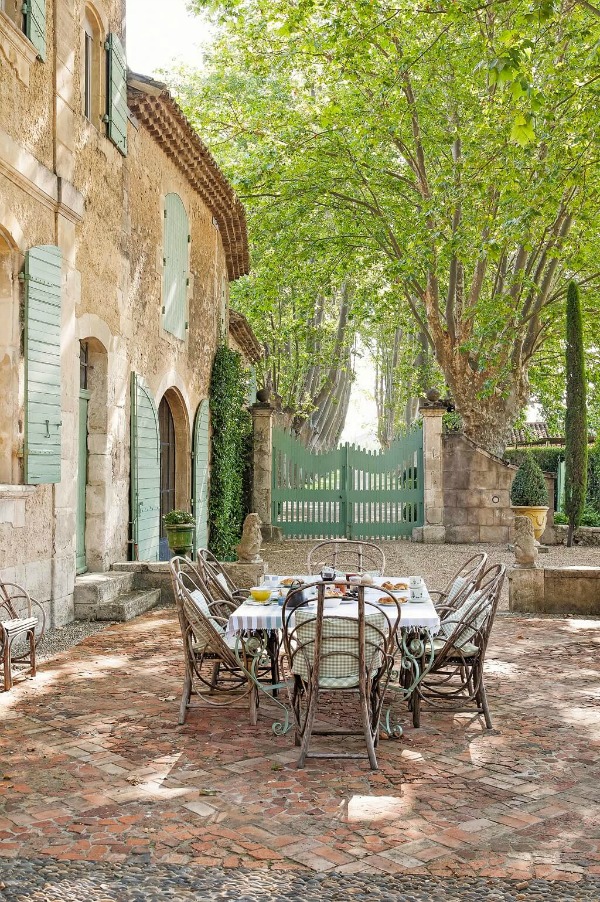 Enchanting French courtyard with traditional outdoor dining furniture, green shutters and gates, and stone facade at a Provence chateau - Haven In.