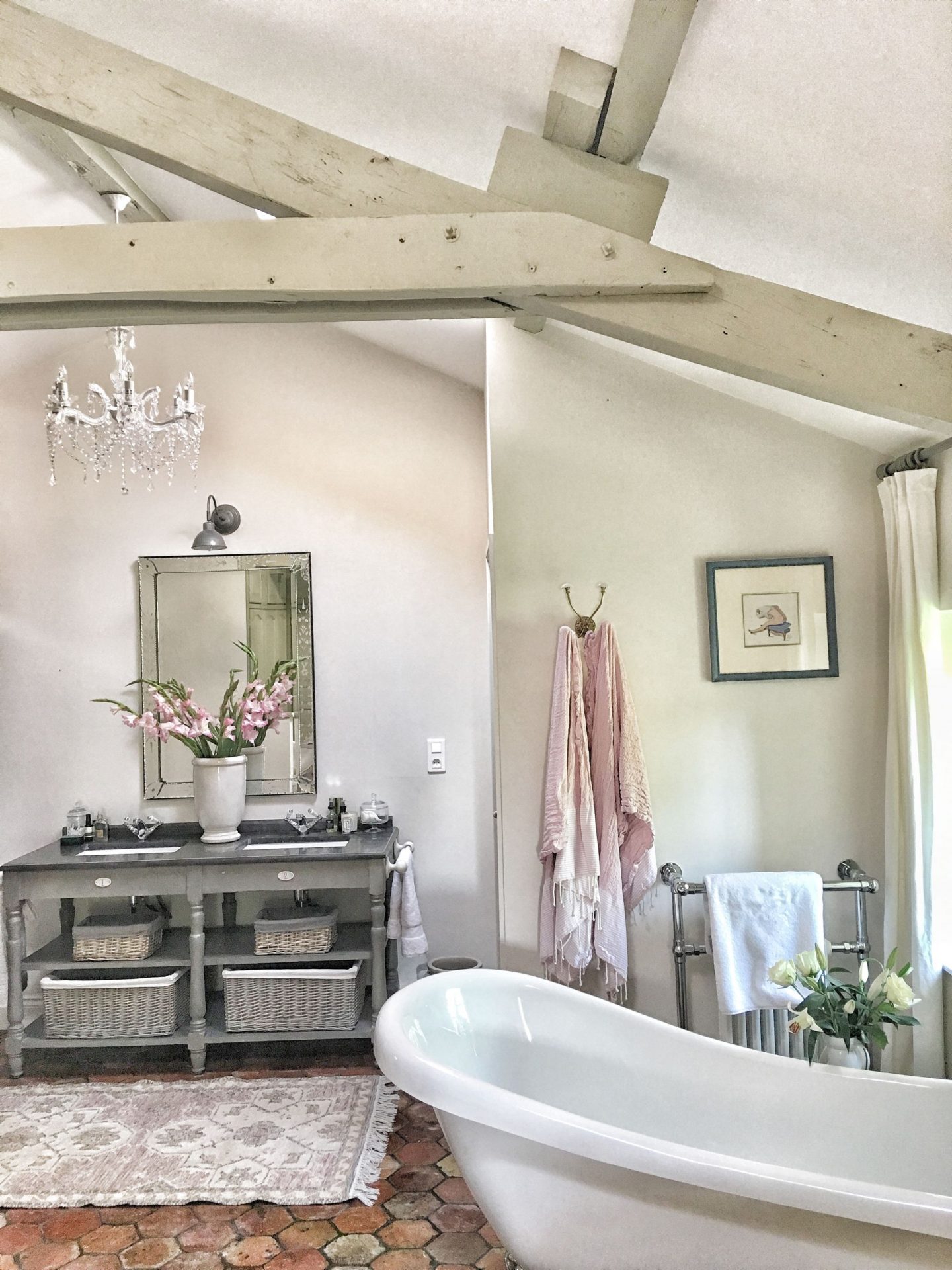 Quiet and timeless hues in a French farmhouse bathroom by Vivi et Margot features reclaimed terracotta hex tiles, freestanding tub, romantic chandelier, and Farrow and Ball's Strong White on the walls.