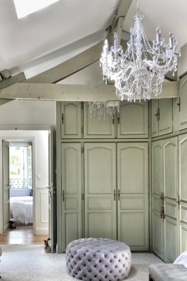 Grand candle style crystal chandelier and built-ins in a French bedroom with tufted ottoman. You'll love this photo gallery and house tour of a home near Bordeaux, France. #vivietmargot #frenchfarmhouse #rusticdecor #countryfrench #interiordesign #bedroomdecor
