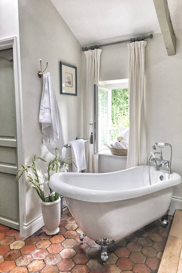 Clawfoot tub and antique terracotta tiles in bath. Enjoy this house tour and ideas to get a rustic European country look! #bathroomdesign #clawfoottub #frenchcountry #farrowandballstrongwhite