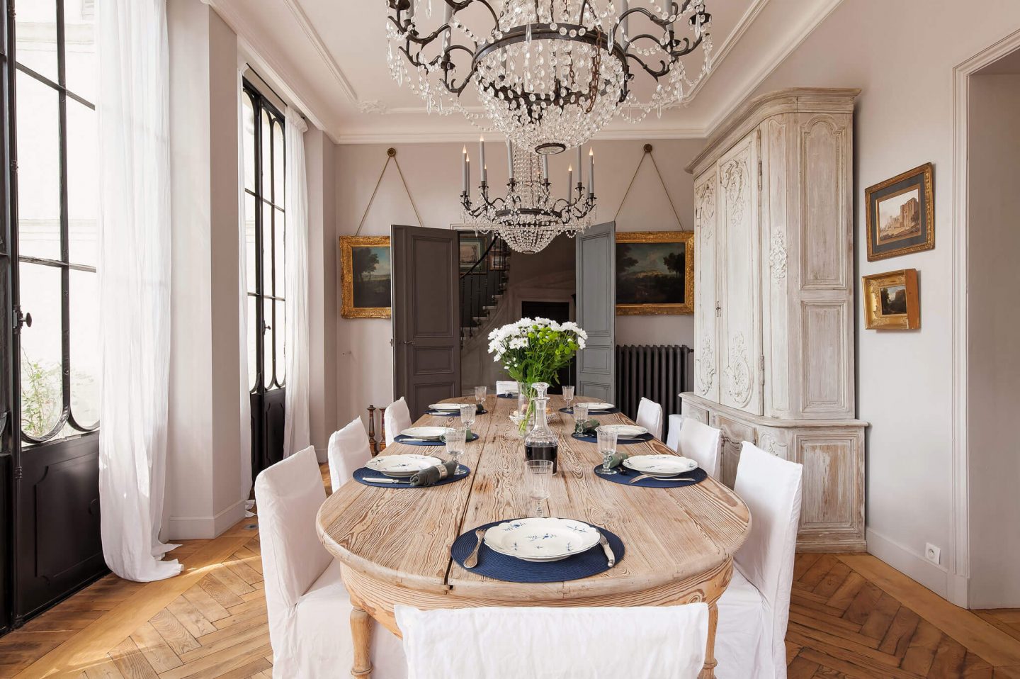 White and serene French dining room with rustic oak farm table. Come see a Breathtaking French Château Tour in Provence With Photo Gallery of Historical Architecture, Dramatic Eclectic Interiors & Oddities!