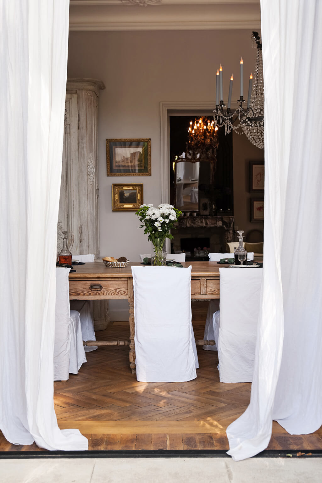 White slipcovered dining chairs with rustic oak farm table in an Avignon dining room. Come see a Breathtaking French Château Tour in Provence With Photo Gallery of Historical Architecture, Dramatic Eclectic Interiors & Oddities!