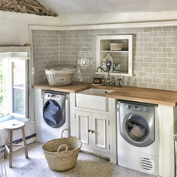 Charming French farmhouse laundry room by Vivi et Margot with farm sink, French laundry basket, tiled wall, and breezy European country style.