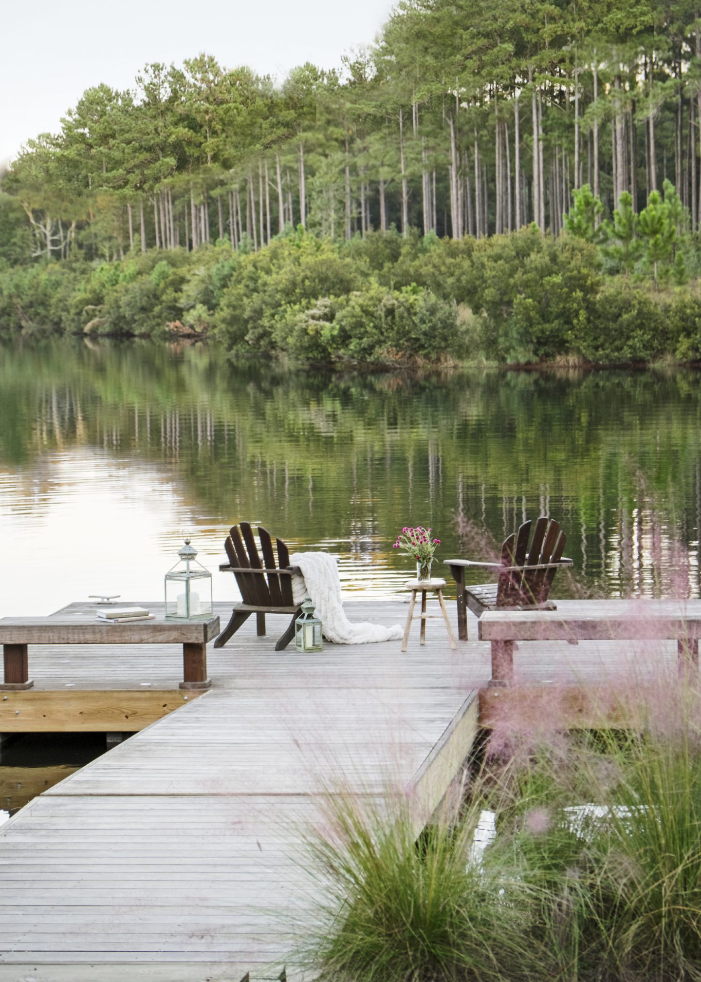 At a Palmetto Bluff property with interior design by Suzanne Kasler, an iconic Low Country dock is the ultimate place to sit, have a drink, and watch the sun rise and set. Adirondack chairs, a rustic three-legged stool, cozy knit throw, and simple lanterns are the recipe for relaxation.