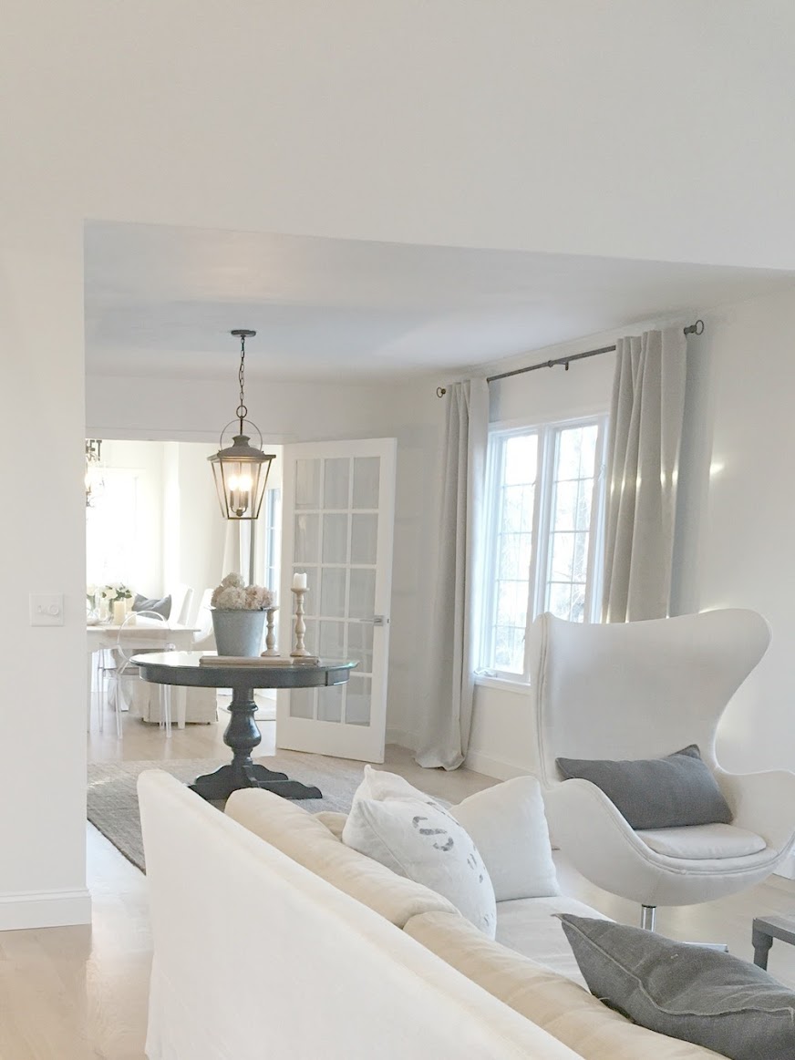 European country inspired neutral living room with white oak flooring, Belgian linen upholstered furniture, and charcoal accents. Walls are Benjamin Moore White. Hello Lovely Studio.