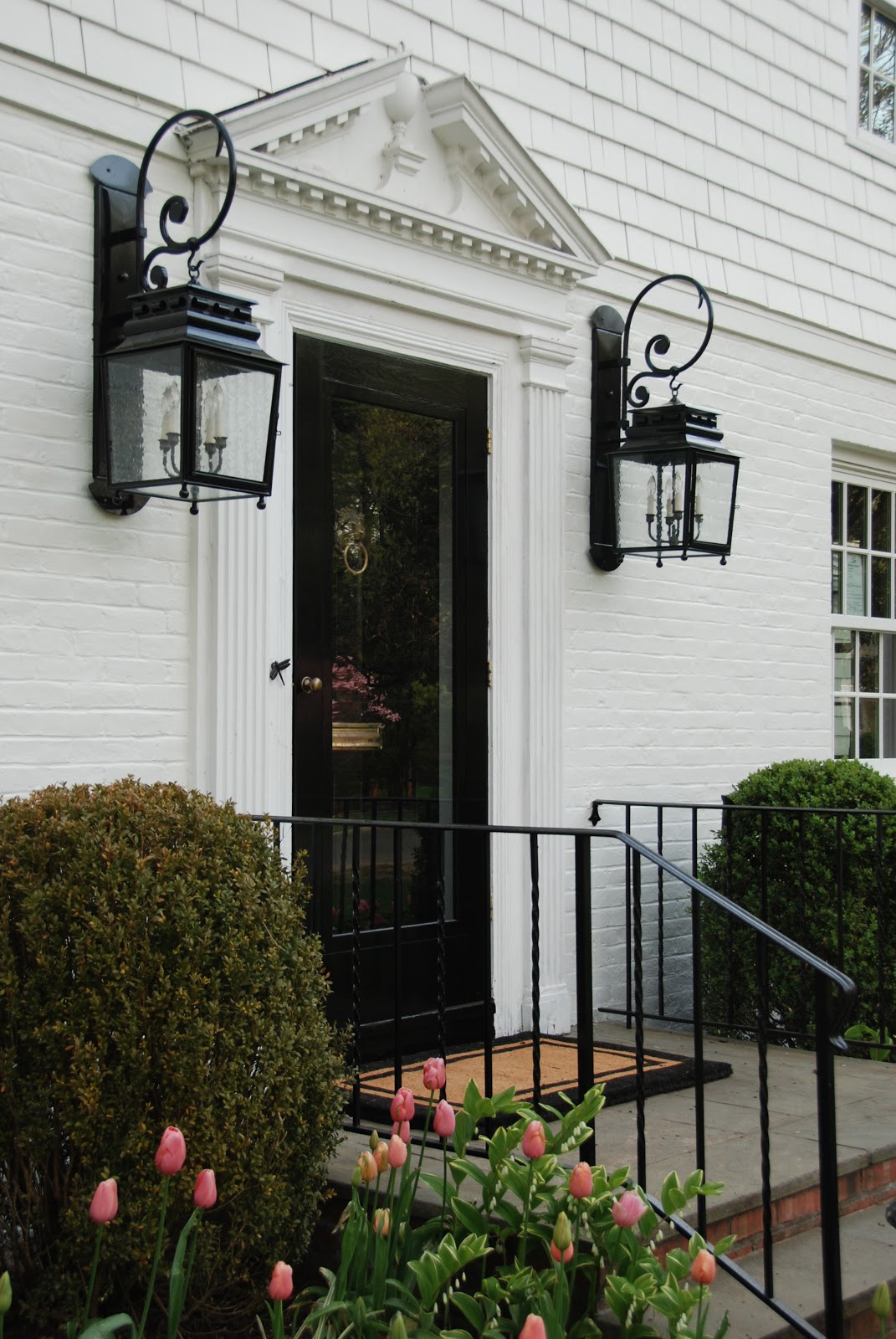 Black front door and lanterns on a traditional and classic white home. Elizabeth of Pretty Pink Tulips. #houseexterior #frontdoor #pinktulips #blackandwhite