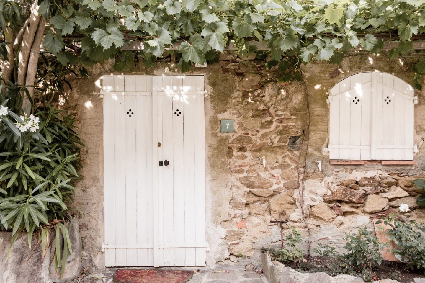 French farmhouse with stone, lush greenery, and white doors. Photo: The Flying Dutchwoman. #frenchfarmhouse #rustic #stone #oldworld #vintagedoors