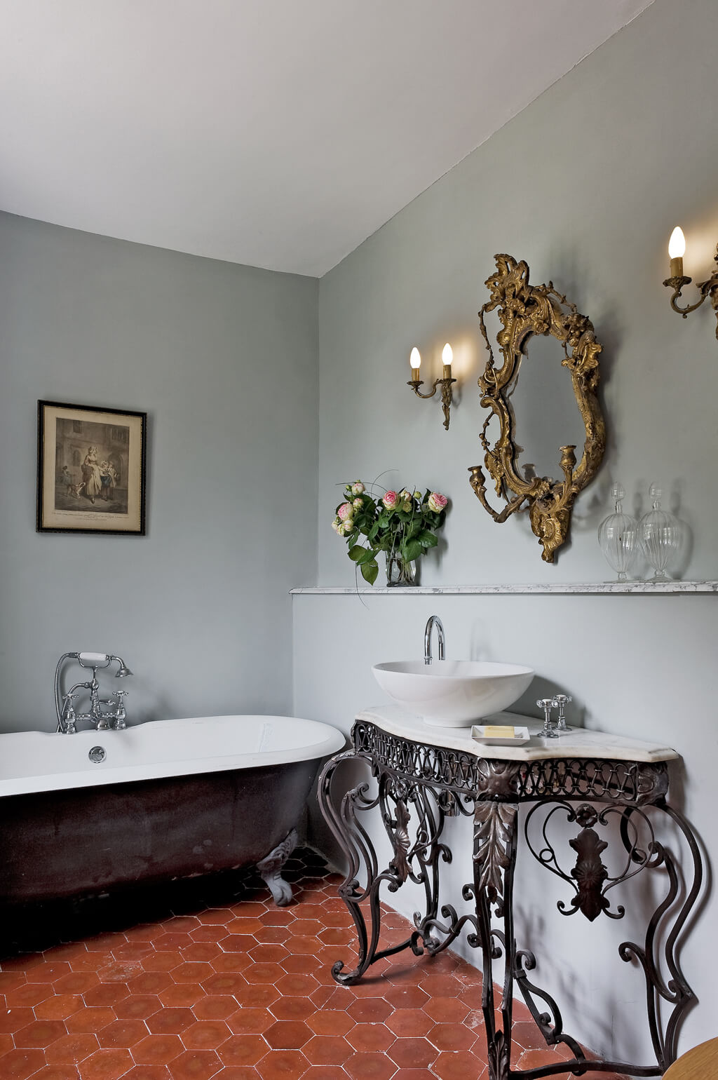 Elegant Old World French bath in Provence chateau with clawfoot tub, hex terracotta tiles, and ornate demilune table - Haven In.