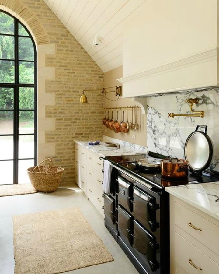 Breathtaking, elegant, and rustic luxe English country kitchen by deVOL kitchens in the UK with bespoke cabinetry, AGA stove, steel windows and doors, woven pendants, and copper accents. Interior design by Susie Atkinson.