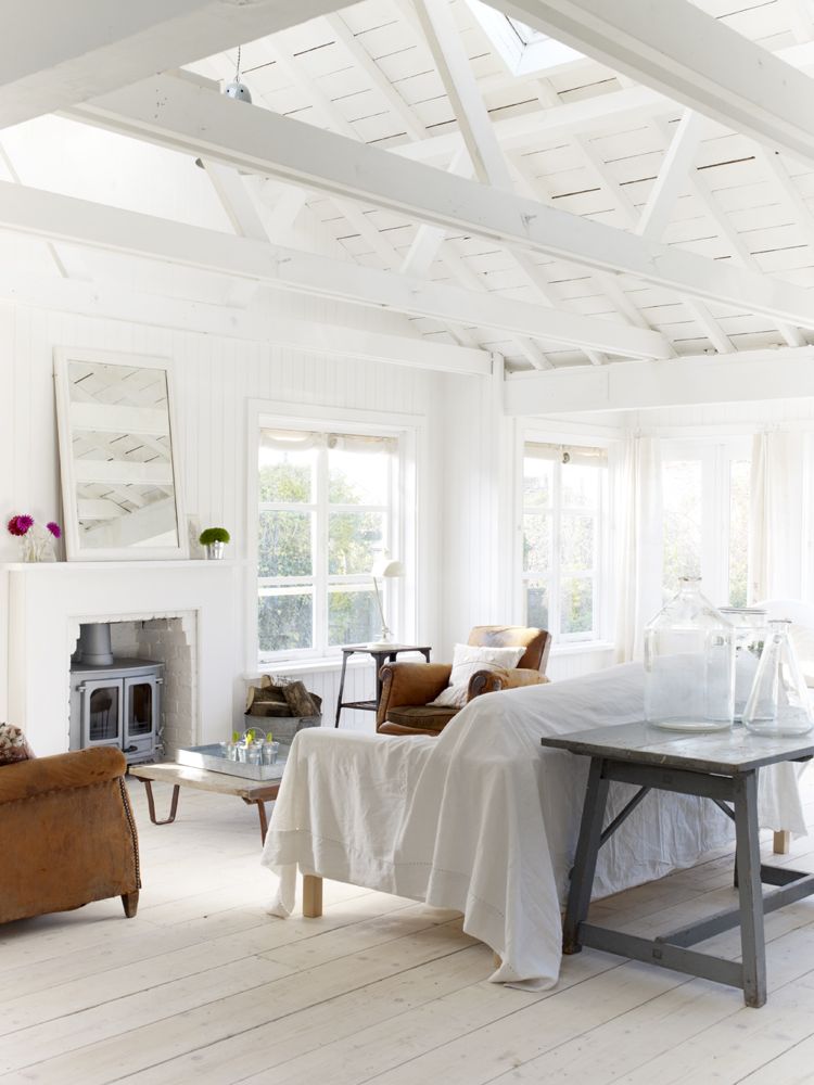 White on white decor in a country cottage living room with unfussy furniture and a wood burning stove placed inside an old fireplace. The Beach Studios.