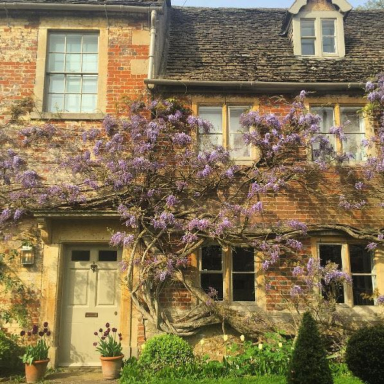 Charming English country cottage with wisteria and weathered brick for a storybook exterior! #Englishcountry #Englishcottage #wisteria #cottageexterior #stonecottage #storybook #houseexterior