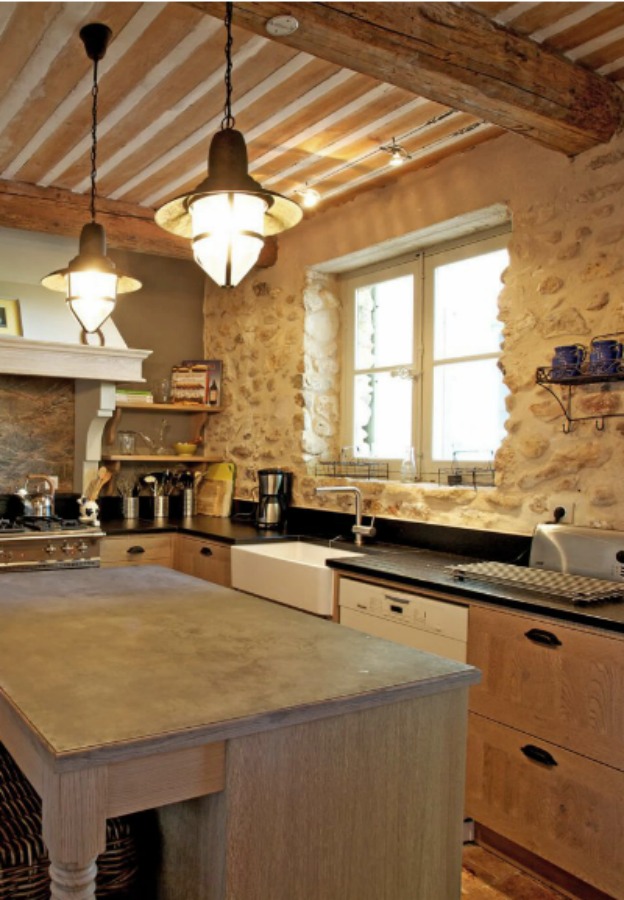 French farmhouse kitchen with rustic stone wall, coastal style pendants, and professional appliances. Provence French country kitchen from a vacation property offered by Haven In.. 