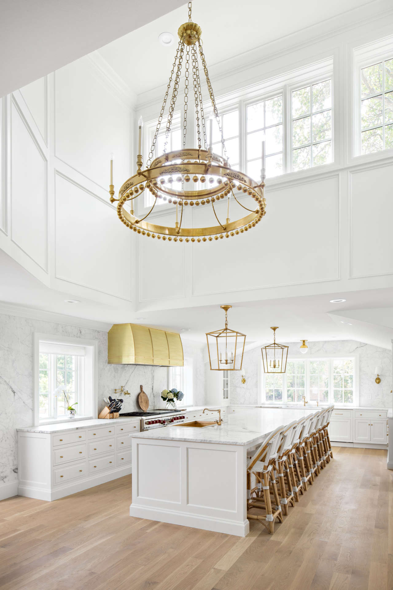 Elegant timeless kitchen design by The Fox Group with soaring ceiling, brass hardware, white oak floors, and white Shaker cabinets.