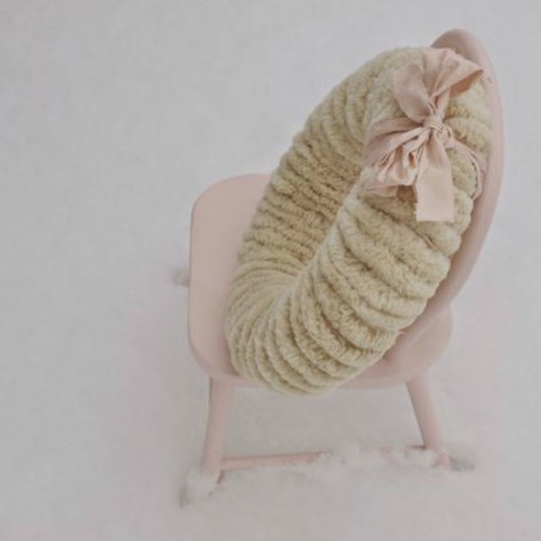 Wooly pom pom wreath on a wee pink chair in the snow by Hello Lovely Studio.