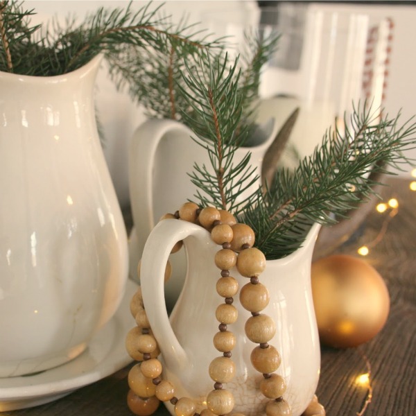 White ironstone pitchers with fresh evergreen sprigs for a farmhouse Christmas decor look by Hello Lovely Studio.