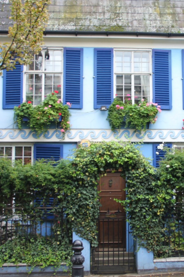 Charming European cottage with royal blue shutters on bright sky blue house exterior with window boxes. Hello Lovely Studio. Notthing Hill home.