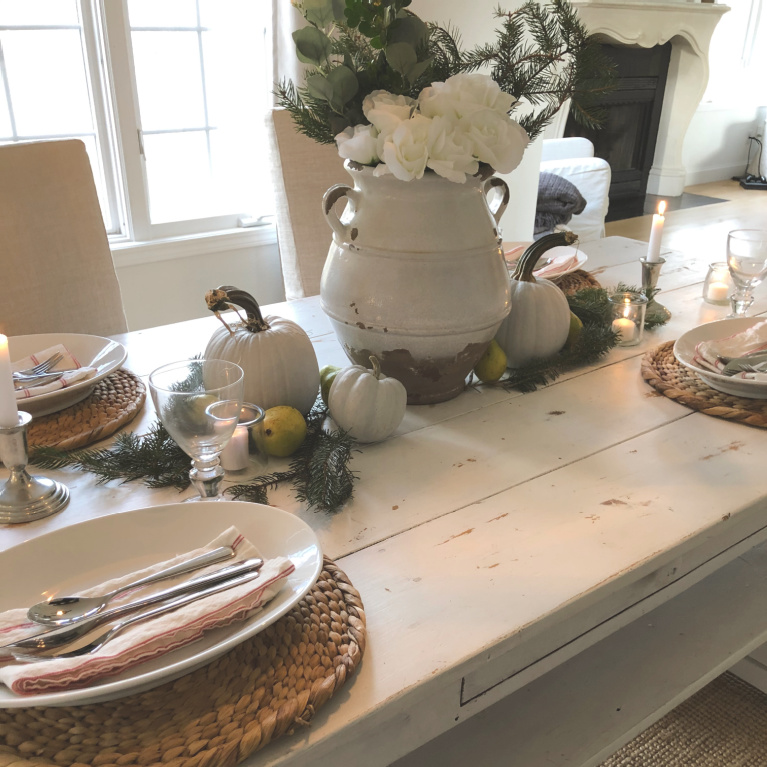 Simple Thanksgiving tablescape with white farm table, pale pumpkins, fresh greenery and candlelight - Hello Lovely Studio.