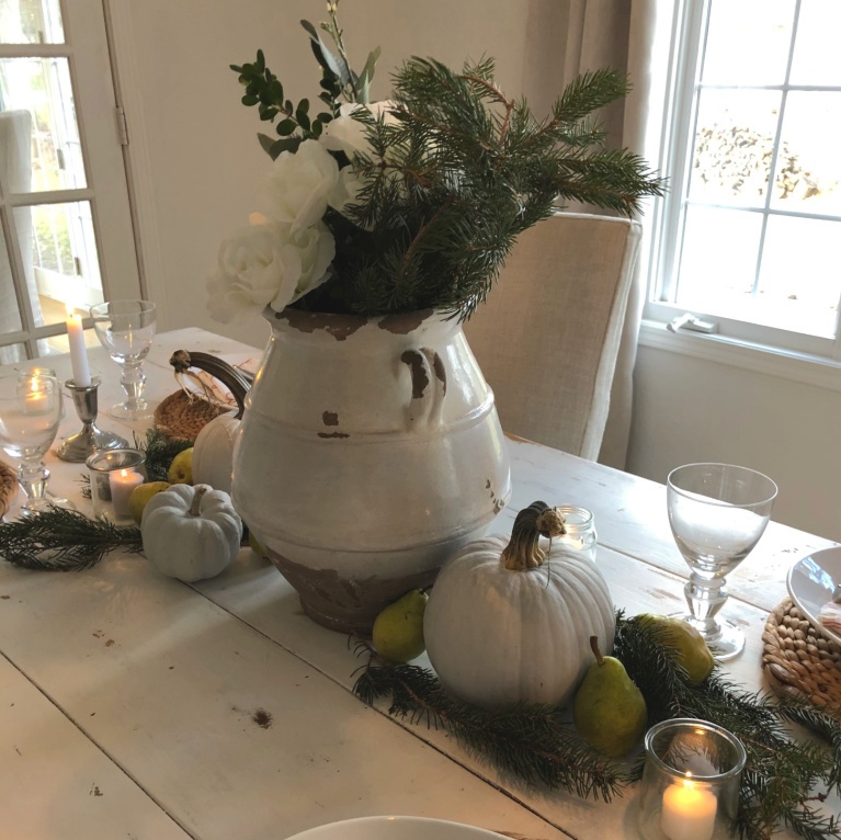 Simple Thanksgiving tablescape with white farm table, pale pumpkins, fresh greenery and candlelight - Hello Lovely Studio.