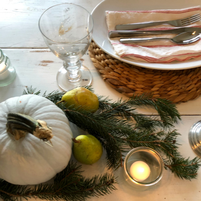 Simple Thanksgiving tablescape with white farm table, pears, pale pumpkins, fresh greenery and candlelight - Hello Lovely Studio.