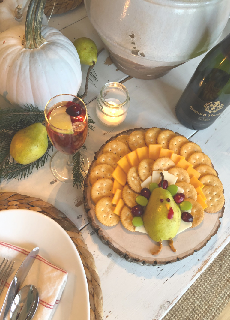 Sweet cheese board with whimsical turkey (made from pear) on our Thanksgiving table with greenery and pale pumpkins - Hello Lovely Studio. #cheeseplatter #thanksgivingrecipes #holidaytable