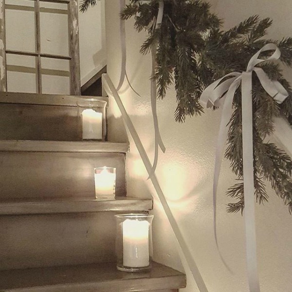 Simple glass hurricanes and whtie candles line a staircase with fresh greenery garland in a French inspired home. #christmasdecor #simplechristmas #frenchcountry #frenchnordic