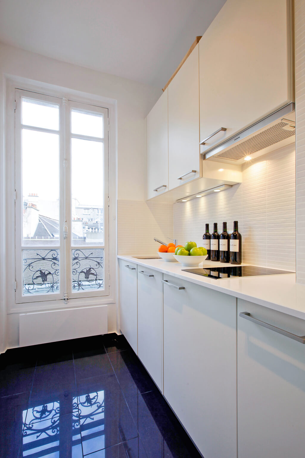 Modern yet timeless Parisian apartment kitchen with polished navy tile floor and white cabinetry - Hello Lovely Studio.