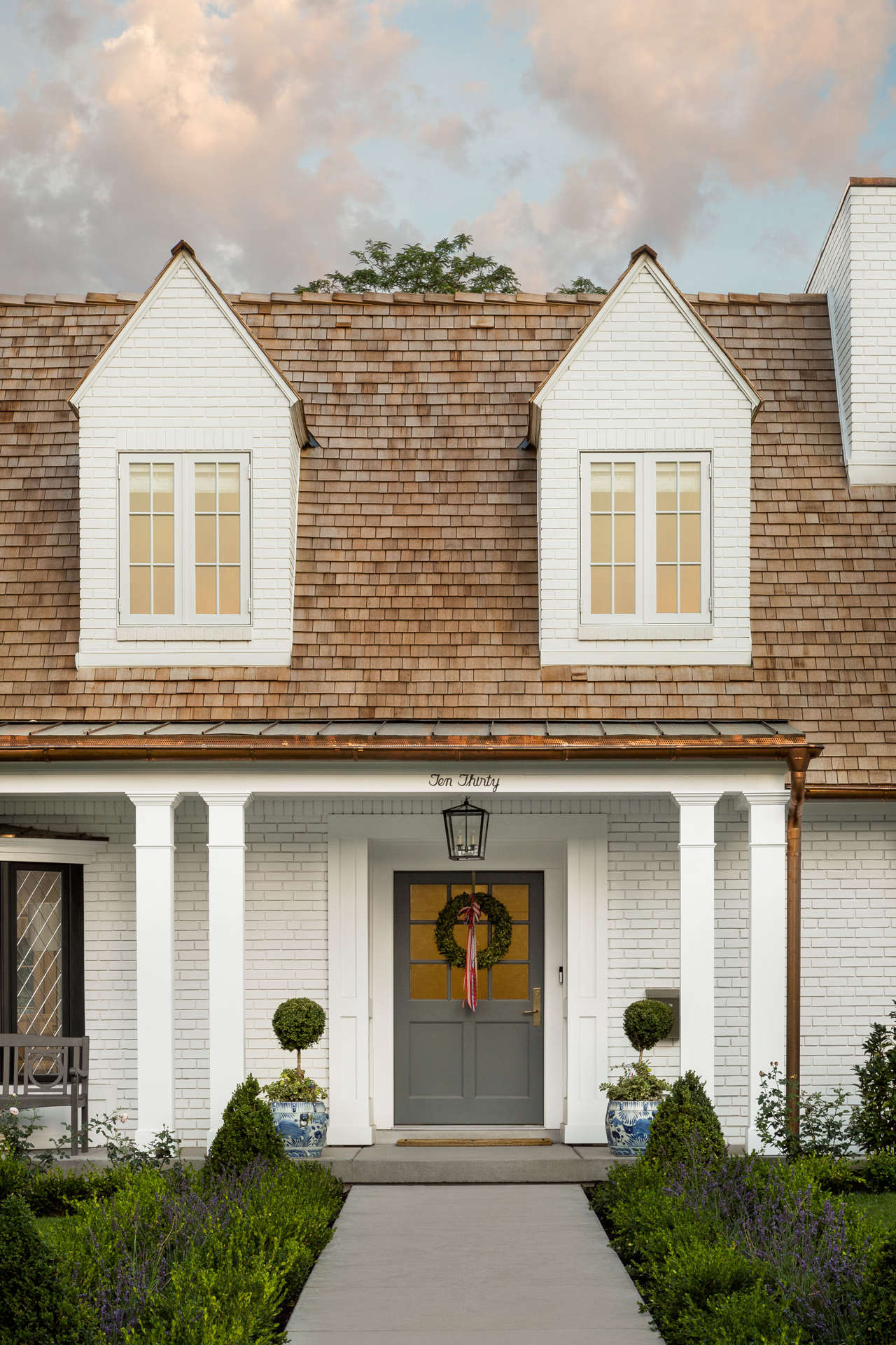 Exterior of a beautiful white brick Tudor home with grey door with wreath. #thefoxgroup #houseexterior #tudor #whitebrick