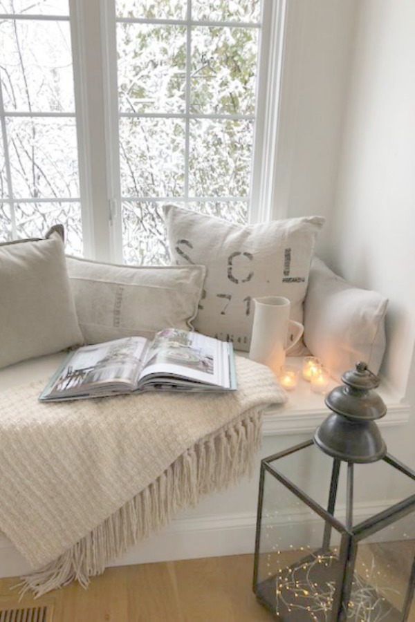White and neutral decor on a window seat bench in a cozy kitchen with candlelight. Hello Lovely Studio.