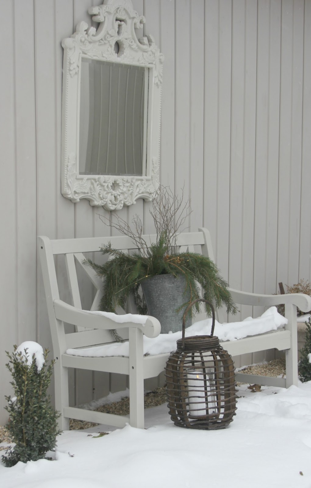 A Nordic French winter vignette with snow, bench, mirror, lantern, and rustic charm. Hello Lovely Studio.