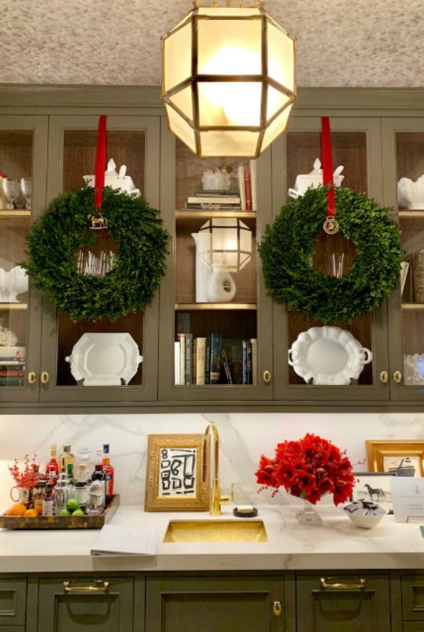 Simple wreaths hung on from kitchen cabinets by solid red ribbon in a showhouse for Christmas decor. Beautiful holiday decor inspiration from interior designers and bloggers. Come discover 28 Amazing Christmas Decorating Ideas! #christmasdecor #holidaydecorating