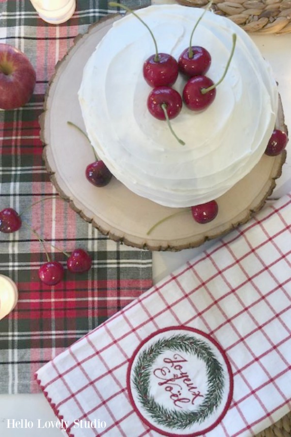 Simple and rustic layer cake on a wood slice decorated for Christmas with cherries. Plaid linens from Urban Farmgirl. Beautiful holiday decor inspiration from interior designers and bloggers. Come discover 28 Amazing Christmas Decorating Ideas! #christmasdecor #holidaydecorating