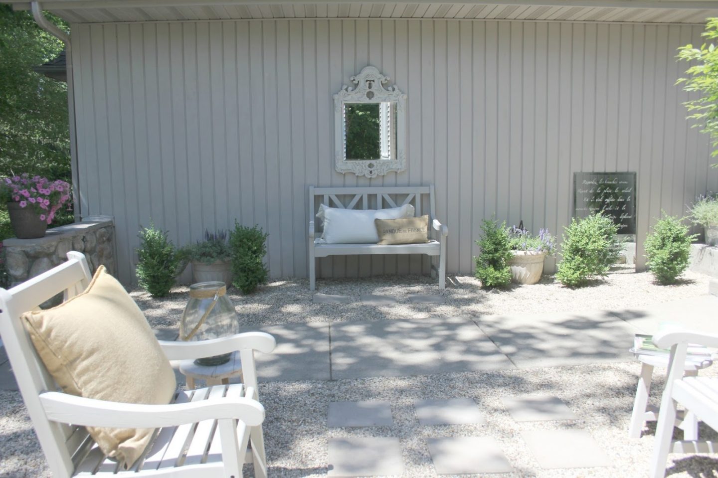 French country courtyard with stone walls, pea gravel, boxwood, lavender, wood furniture, and vintage touches. Come see the before and after of our project on Hello Lovely Studio. #hellolovelystudio #frenchcountry #courtyard #gardeninspiration #renovation 