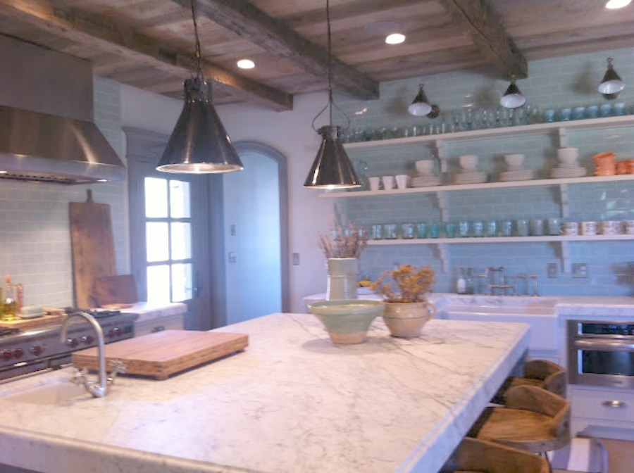 Open shelving and green glazed subway tile backsplash in a Gustavian French farmhouse kitchen by Decor de Provence with center island and farmhouse pendant lighting.