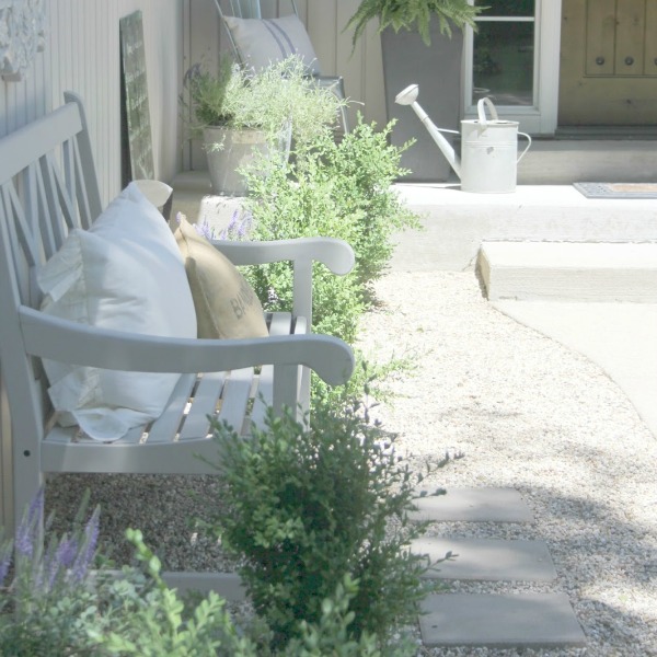 French country courtyard with stone walls, pea gravel, boxwood, lavender, wood furniture, and vintage touches. Come see the before and after of our project on Hello Lovely Studio. #hellolovelystudio #frenchcountry #courtyard #gardeninspiration #renovation 