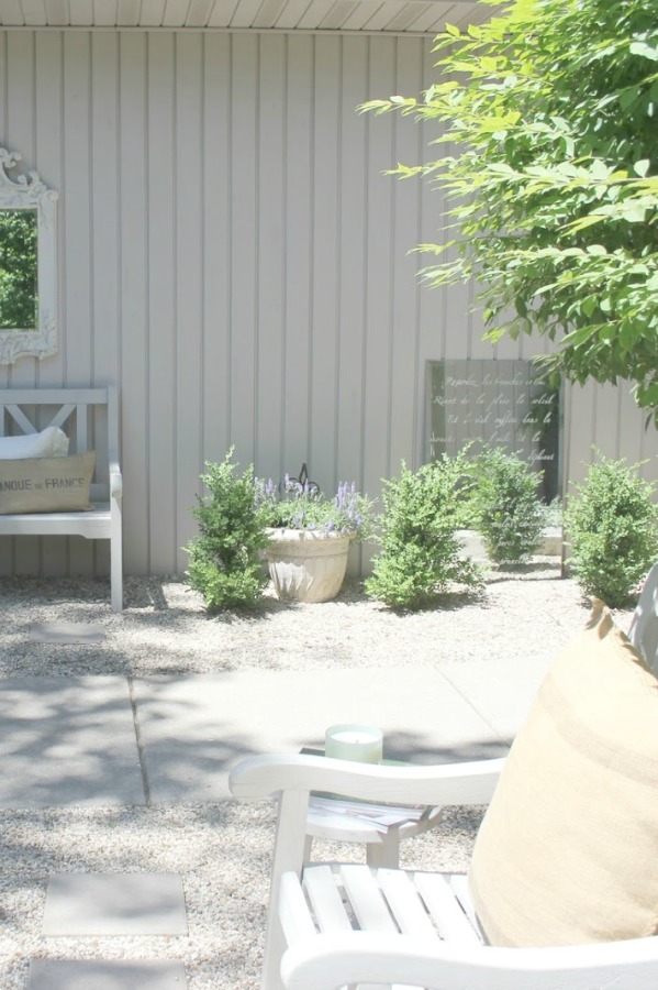 French country courtyard with stone walls, pea gravel, boxwood, lavender, wood furniture, and vintage touches. Come see the before and after of our project on Hello Lovely Studio. #hellolovelystudio #frenchcountry #courtyard #gardeninspiration #renovation 