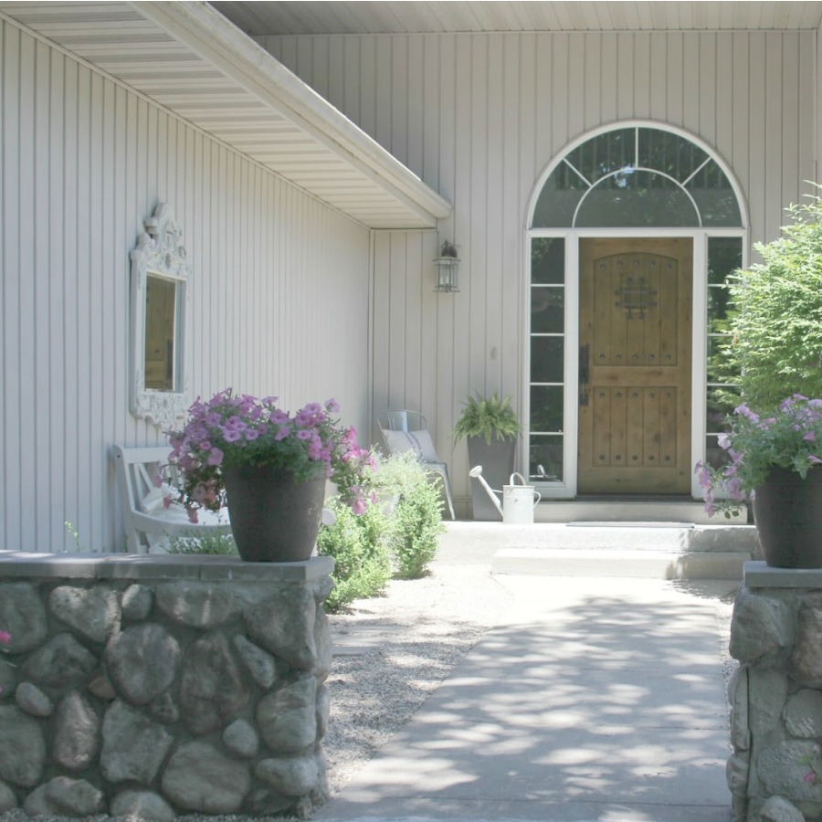 French country courtyard with stone walls, pea gravel, boxwood, lavender, wood furniture, and vintage touches. Come see the before and after of our project on Hello Lovely Studio. #hellolovelystudio #frenchcountry #courtyard #gardeninspiration #renovation 