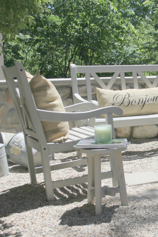 French country courtyard with stone walls, pea gravel, boxwood, lavender, wood furniture, and vintage touches. Come see the before and after of our project on Hello Lovely Studio. #hellolovelystudio #frenchcountry #courtyard #gardeninspiration #renovation 