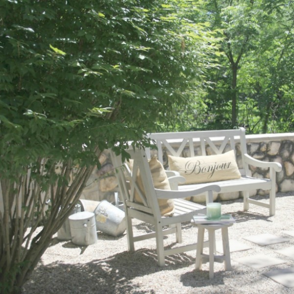 French country courtyard with stone walls, pea gravel, boxwood, lavender, wood furniture, and vintage touches. Come see the before and after of our project on Hello Lovely Studio. #hellolovelystudio #frenchcountry #courtyard #gardeninspiration #renovation