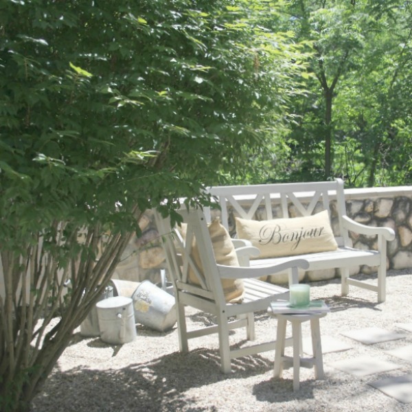 French country courtyard with stone walls, pea gravel, boxwood, lavender, wood furniture, and vintage touches. Come see the before and after of our project on Hello Lovely Studio. #hellolovelystudio #frenchcountry #courtyard #gardeninspiration #renovation 