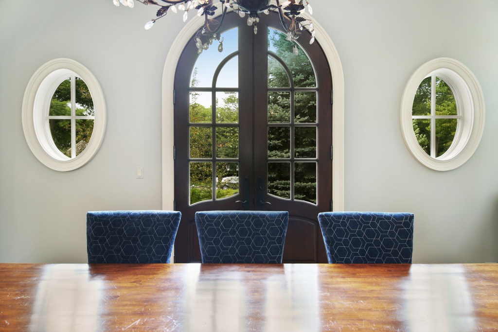 Oval windows and arched French doors in a dining room painted a soothing pale blue in a grand Hinsdale manse. Come explore more Country French Decor Ideas from luxurious and grand homes.