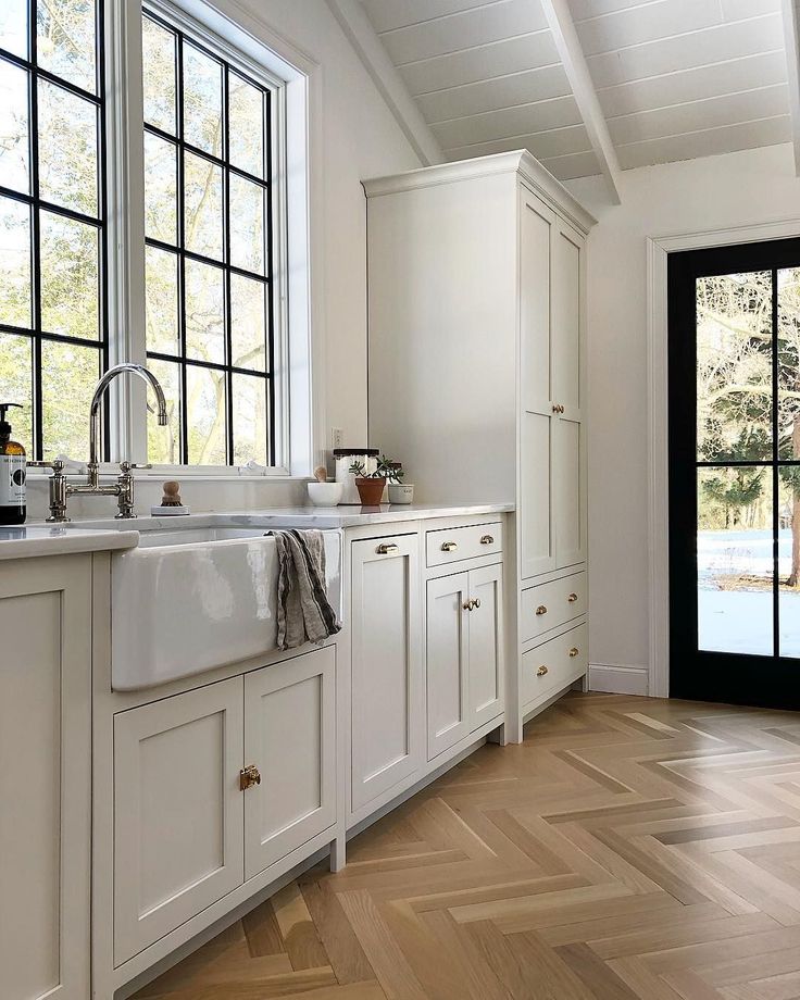 Beautiful white modern farmhouse kitchen with black accents, farm sink, and herringbone wood flooring - Simple Offerings. #whitekitchen #herringbonewoodflooring #modernfarmhousekitchen #shakerkitchen